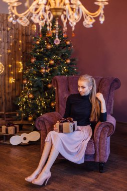 Bir kazak ve koltuk hediye kutusunda el ile Noel ağacı yanında oturan etek giymiş genç kadın güzel.
