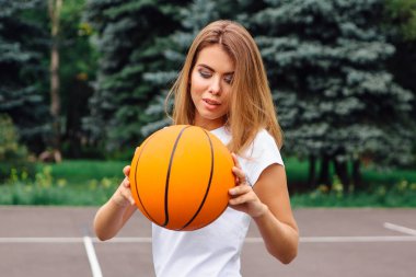 Güzel genç kız beyaz tişört, şort ve spor ayakkabısı, giyinmiş bir basketbol sahası üzerinde bir top ile çalış.