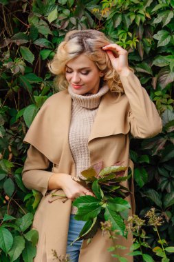 Kazak ve ceket genç güzel kadın sonbahar yaprakları buket tutan yabani üzüm arka plan yanında duruyor