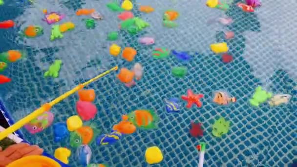 Les enfants attrapent des cannes à pêche poissons en plastique coloré dans une piscine jouet . — Video