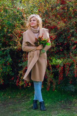 Beautiful elegant woman standing next barberry bush in autumn park clipart