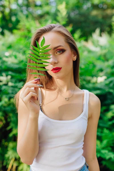 Retrato de mujer con hermosos ojos verdes vestida con camisa blanca con una hoja cerca de un ojo . — Foto de Stock