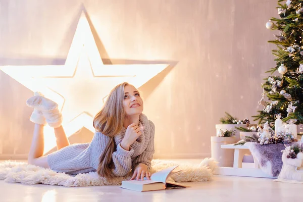 La mujer hermosa joven que pone y que lee el libro bajo el árbol de Navidad en el interior de fiesta —  Fotos de Stock