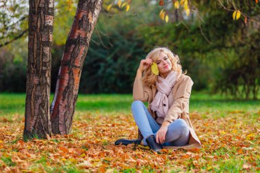 Zemin örtmek ile düşmüş sonbahar üzerinde oturan genç güzel kadın bırakır