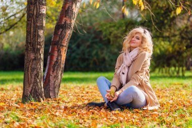 Zemin örtmek ile düşmüş sonbahar üzerinde oturan genç güzel kadın bırakır