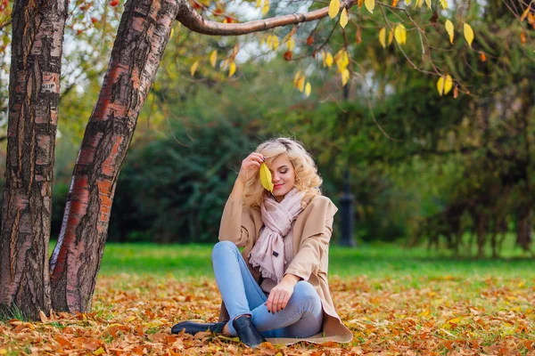 Młoda piękna kobieta siedziała na coverd ziemi z fallen jesieni pozostawia — Zdjęcie stockowe