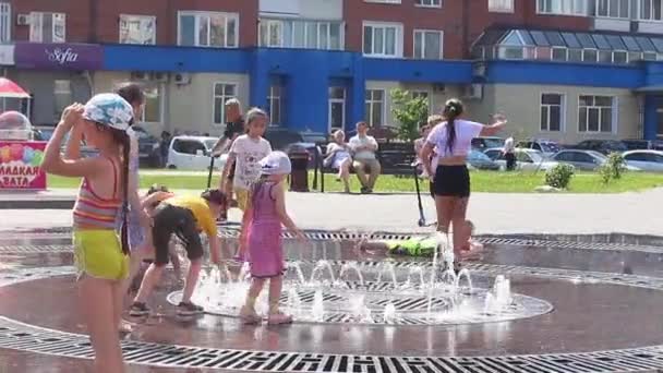 Novokuznetsk, Región de Kemerovo, Rusia - 28 de junio de 2019: Adolescentes felices salpicando en el agua de una fuente de la ciudad y disfrutando de los frescos arroyos de agua en un día caluroso . — Vídeo de stock