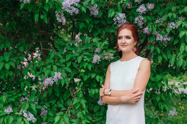 Encantadora mujer vestida con hermoso vestido blanco de pie junto al arbusto lila. Copiar espacio . — Foto de Stock