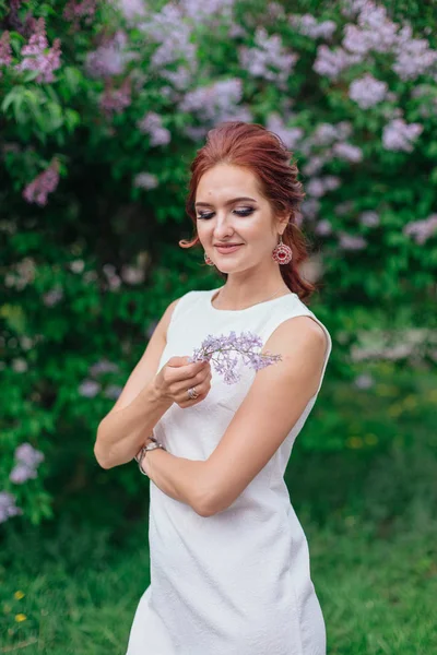 Charmante vrouw het dragen van mooie witte jurk staande naast Lila Bush — Stockfoto