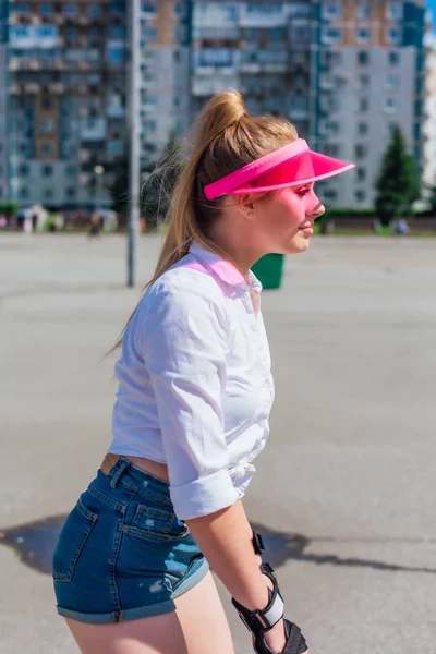 一个情绪化的女孩在粉红色的帽子遮阳板和保护手套的滚轴和滑板的肖像. — 图库照片