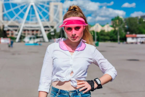 Potret seorang gadis emosional dengan topi merah muda dan sarung tangan pelindung untuk rollerblades dan skateboard . — Stok Foto