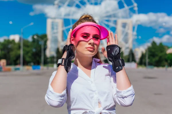 Potret seorang gadis emosional dengan topi merah muda dan sarung tangan pelindung untuk rollerblades dan skateboard . — Stok Foto