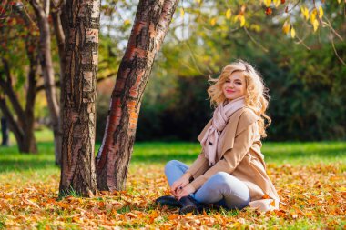 Zemin örtmek ile düşmüş sonbahar üzerinde oturan genç güzel kadın bırakır