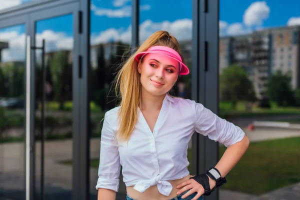 Potret seorang gadis emosional dengan topi merah muda dan sarung tangan pelindung untuk rollerblades dan skateboard . — Stok Foto