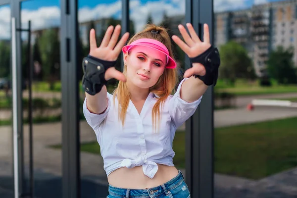 Retrato de una chica emocional con una visera de gorra rosa y guantes protectores para patines y skateboarding . — Foto de Stock