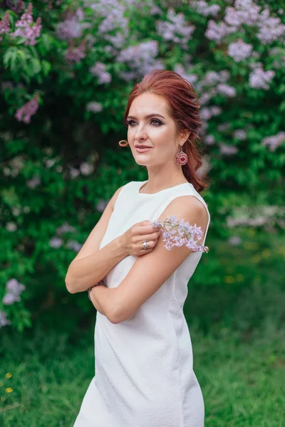 Encantadora mujer con hermoso vestido blanco de pie junto al arbusto lila — Foto de Stock