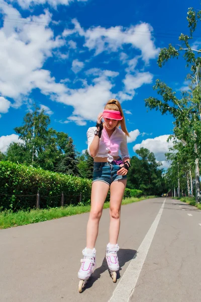 Retrato de una chica emocional en una visera de gorra rosa y guantes protectores para patines y patinetas montadas en patines en la carretera . — Foto de Stock