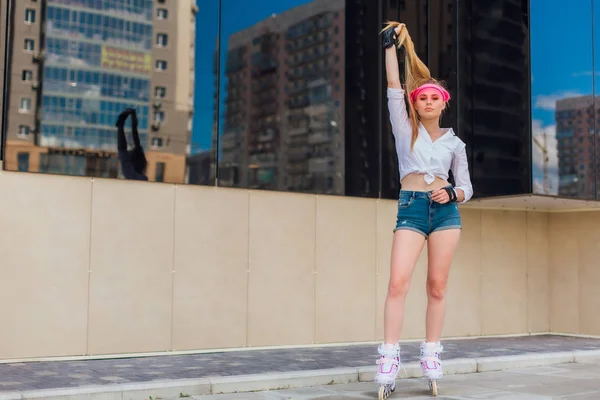 Potret seorang gadis emosional dalam topi merah muda dan sarung tangan pelindung untuk rollerblades dan skateboarding naik rollerblades di jalan . — Stok Foto