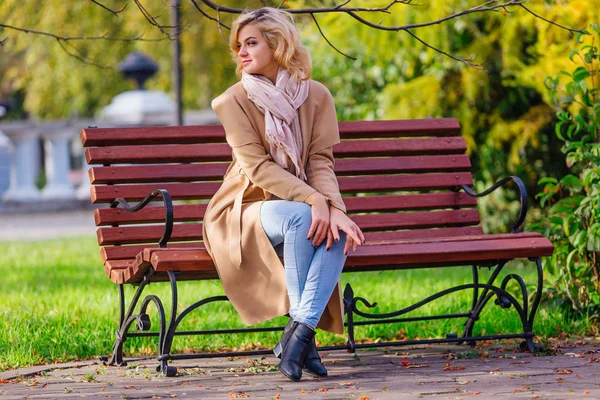 Jovem bela mulher sentada no banco no parque de outono — Fotografia de Stock