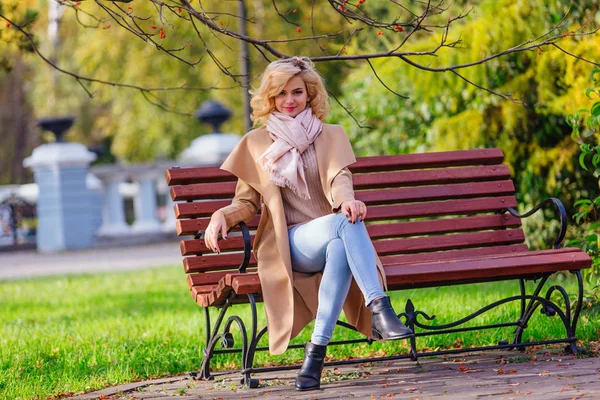 Jonge mooie vrouw zittend op de Bank in herfst Park — Stockfoto