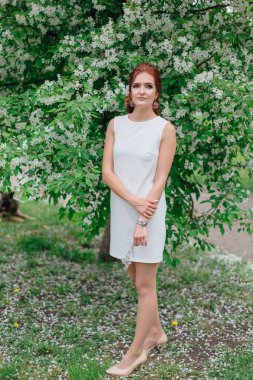 Elma ağacının altında ayakta güzel beyaz elbise giyen büyüleyici kadın