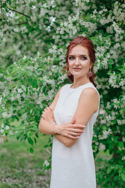 Mujer encantadora vistiendo hermoso vestido blanco de pie bajo el manzano — Foto de Stock