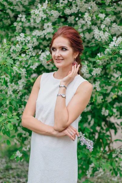Mujer encantadora vistiendo hermoso vestido blanco de pie bajo el manzano —  Fotos de Stock