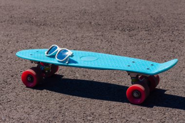Pembe tekerlekler ile mavi plastik kaykay Penny board üzerinde güneş gözlüğü.