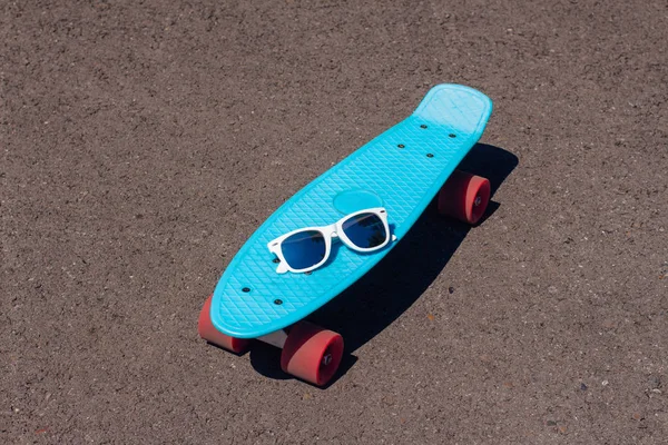 Pembe tekerlekler ile mavi plastik kaykay Penny board üzerinde güneş gözlüğü. — Stok fotoğraf
