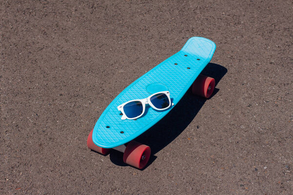 Sunglasses on a blue plastic skateboard penny board with pink wheels.