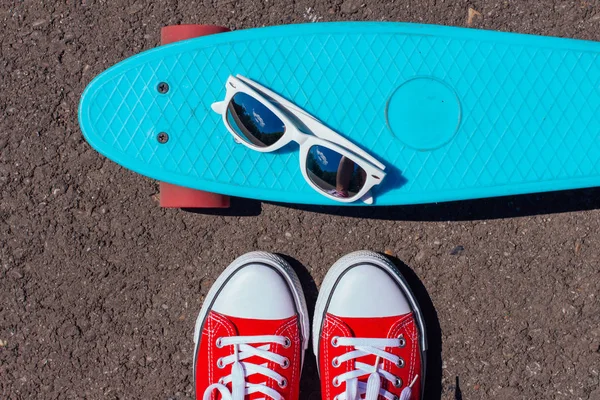 Nahaufnahme von Füßen und Spiegelsonnenbrille auf einem blauen Penny-Skateboard mit rosa Rädern. — Stockfoto