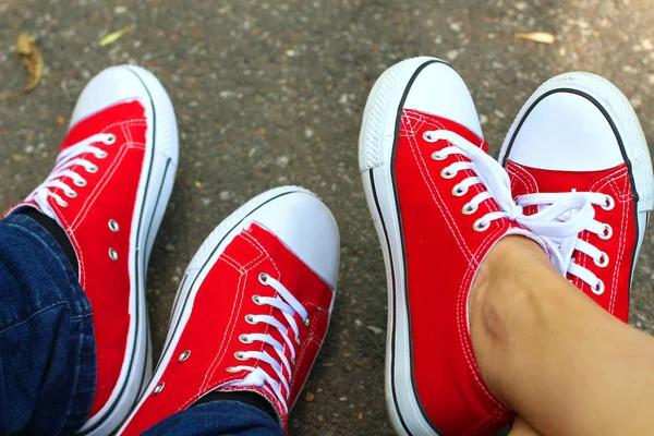 Red sneakers shoes on woman's and man's feet.