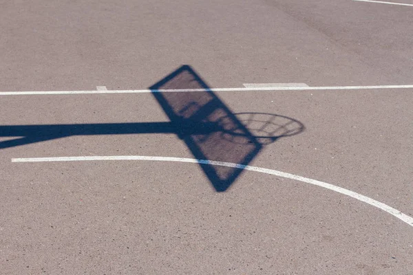 Тень уличного баскетбольного борта с кольцом и сеткой на асфальтированном спортплощадке в городе — стоковое фото