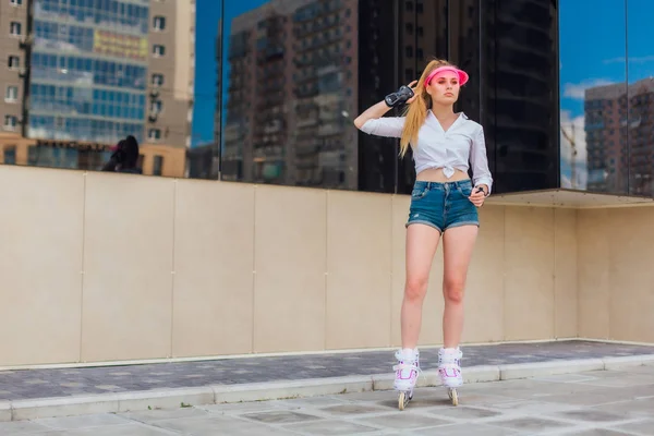 Potret seorang gadis emosional dalam topi merah muda dan sarung tangan pelindung untuk rollerblades dan skateboarding naik rollerblades di jalan . — Stok Foto