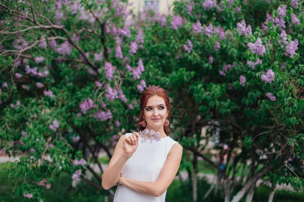 Charmante vrouw draagt prachtige witte jurk staan naast Lila Bush. Ruimte kopiëren. — Stockfoto