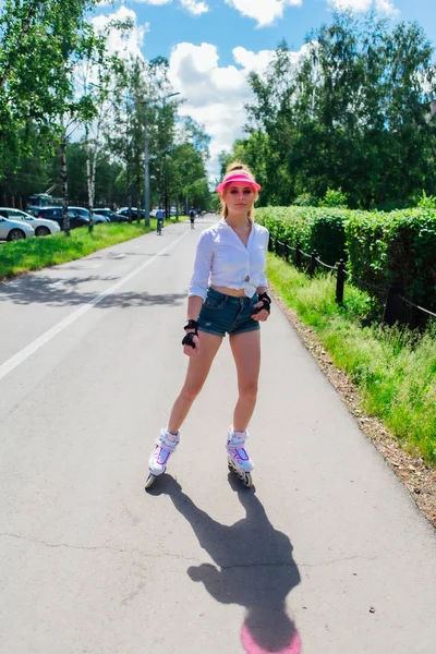 Portret emocjonalnej dziewczyny w różowym daszkiem i rękawice ochronne do rolek i skateboardingu jazda na rolkach na drodze. — Zdjęcie stockowe