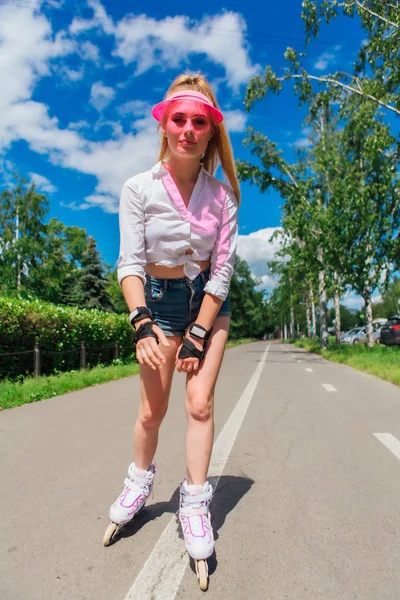 Retrato de una chica emocional en una visera de gorra rosa y guantes protectores para patines y patinetas montadas en patines en la carretera . — Foto de Stock