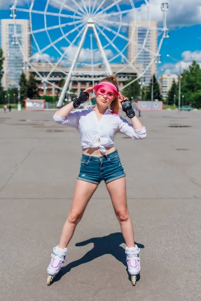 Retrato de una chica emocional en una visera de gorra rosa y guantes protectores para patines y patinetas montadas en patines en la carretera . —  Fotos de Stock