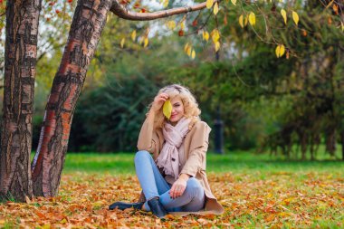 Zemin örtmek ile düşmüş sonbahar üzerinde oturan genç güzel kadın bırakır