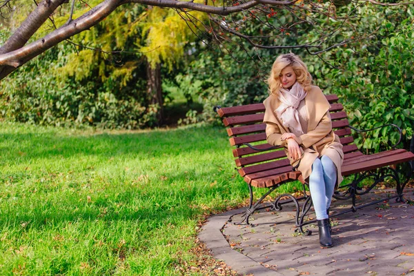 Jovem bela mulher sentada no banco no parque de outono — Fotografia de Stock