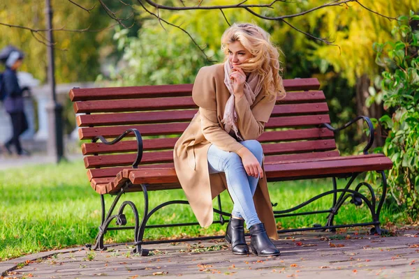 Joven hermosa mujer sentada en el banco en el parque de otoño — Foto de Stock