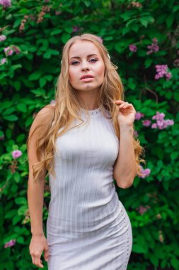 Leylak çalıyanında duran güzel beyaz elbise giyen büyüleyici sarışın bir kadın portresi.