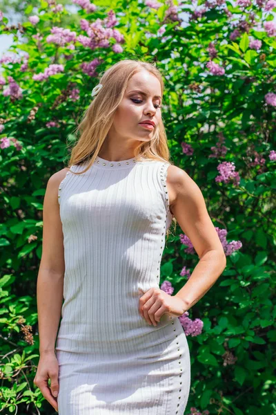 Portret van een charmante blonde vrouw het dragen van mooie witte jurk staande naast Lila Bush. — Stockfoto