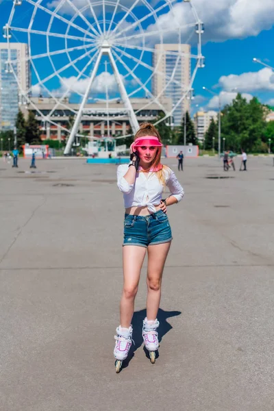 Potret seorang gadis emosional dalam topi merah muda dan sarung tangan pelindung untuk rollerblades dan skateboarding naik rollerblades di jalan . — Stok Foto