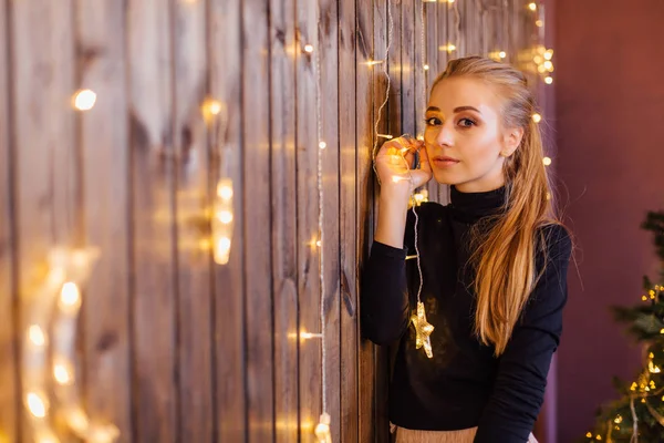 Yıldız ve ay ışıkları ile ahşap duvarın yanında duran bir kazak ve etek giymiş güzel genç kadın