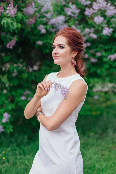 Urocza kobieta ubrana w piękną białą sukienkę stojącą obok krzewu bzu — Zdjęcie stockowe