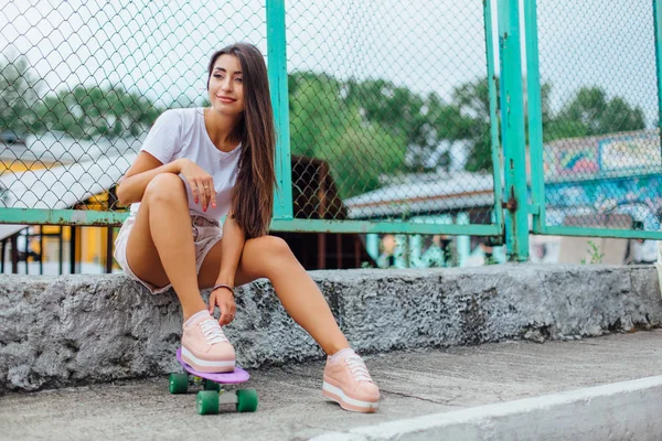 Sommaren livsstil bild av trendiga ganska ung flicka sitter bredvid den skateboard t.ex med hennes plast skateboard. — Stockfoto