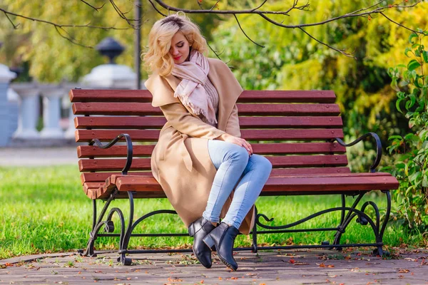 Joven hermosa mujer sentada en el banco en el parque de otoño — Foto de Stock