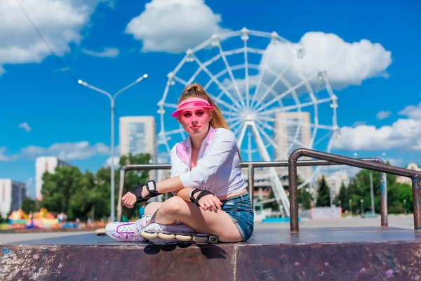 관람차를 배경으로 보호 장갑과 롤러블레이드를 착용한 분홍색 캡 바이저를 입은 감성적인 소녀의 초상화. — 스톡 사진