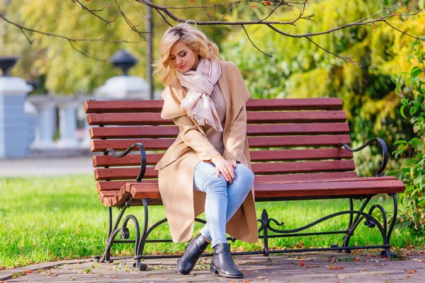 Junge schöne Frau sitzt auf der Bank im Herbstpark — Stockfoto